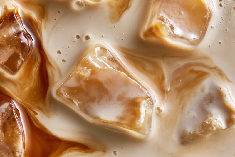 Iced coffee surface with swirling cream and ice cubes in close-up view