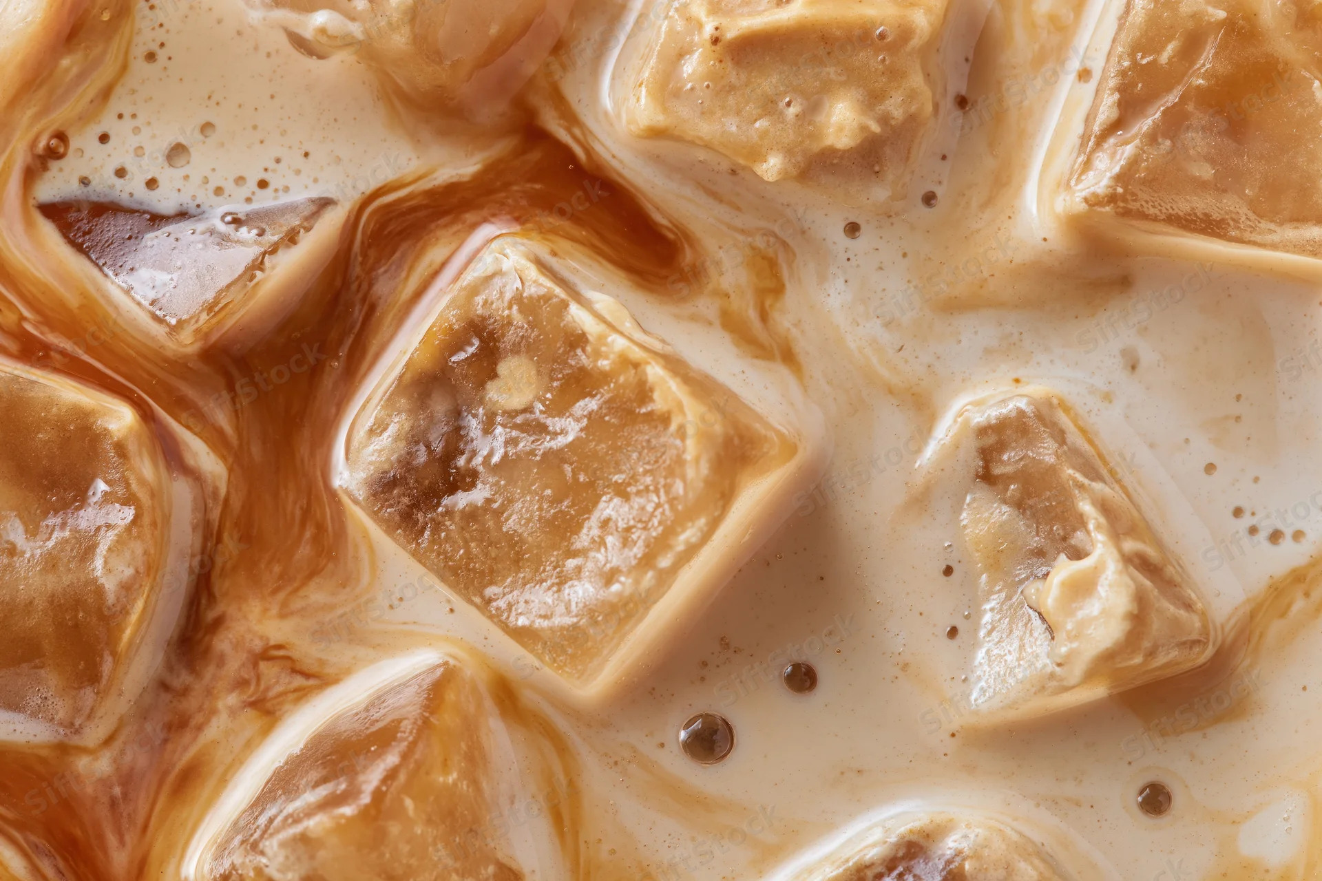 Iced coffee surface with floating ice cubes and swirling cream in close-up view