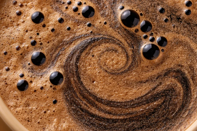 Overhead closeup of black coffee foam with swirling pattern and glossy bubbles