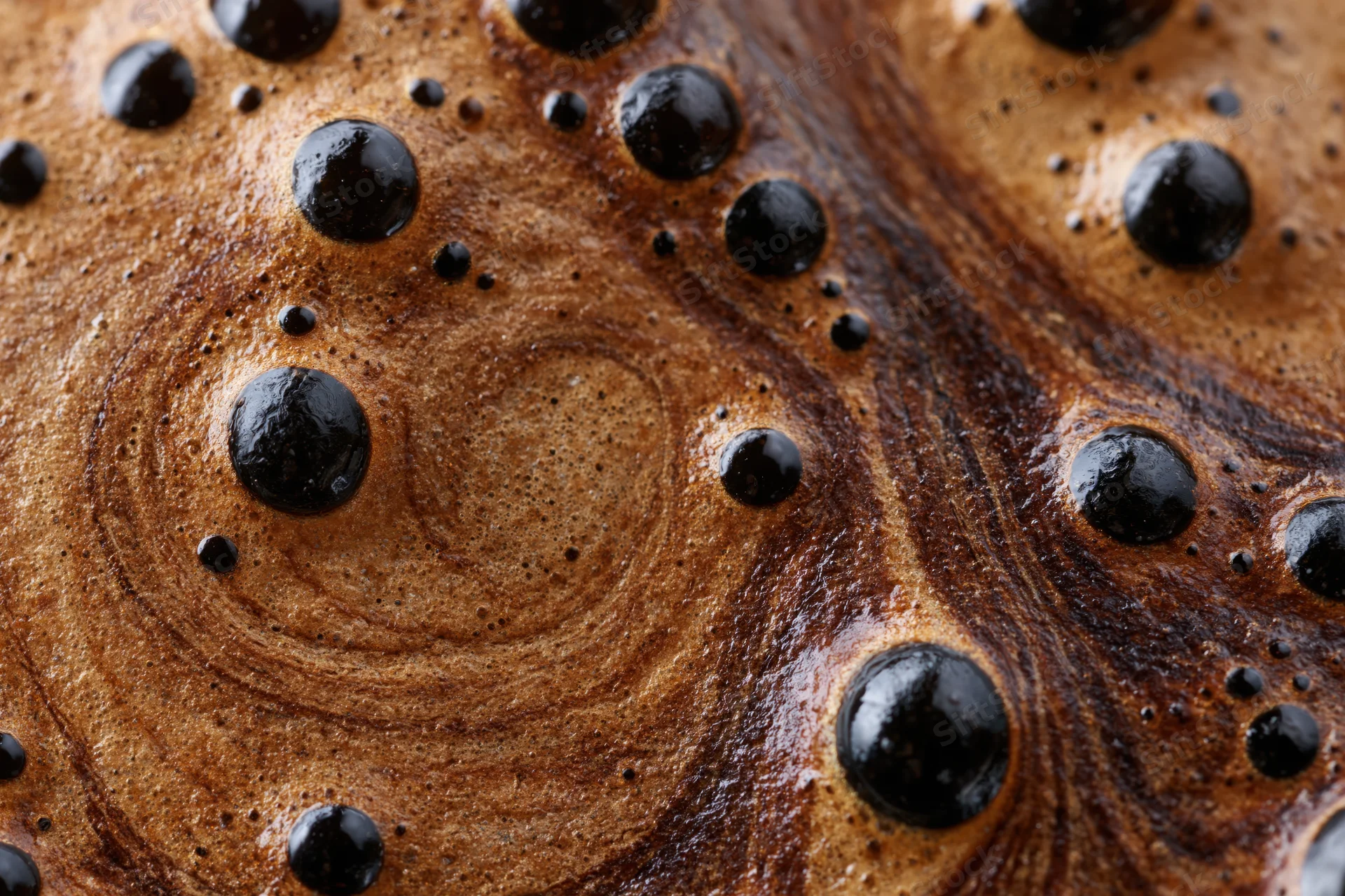 Extreme close-up of black coffee crema with bubbles and swirls on surface