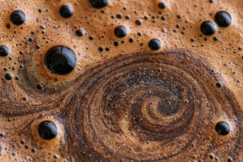 Close-up of swirling black coffee foam with bubbles and glossy surface