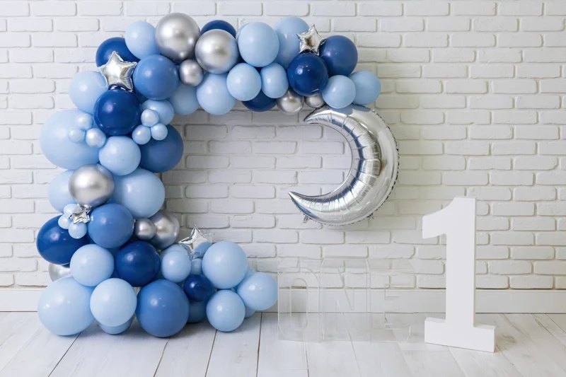 Blue and silver balloon arch with moon and star shapes and a white number one sign against a white brick wall
