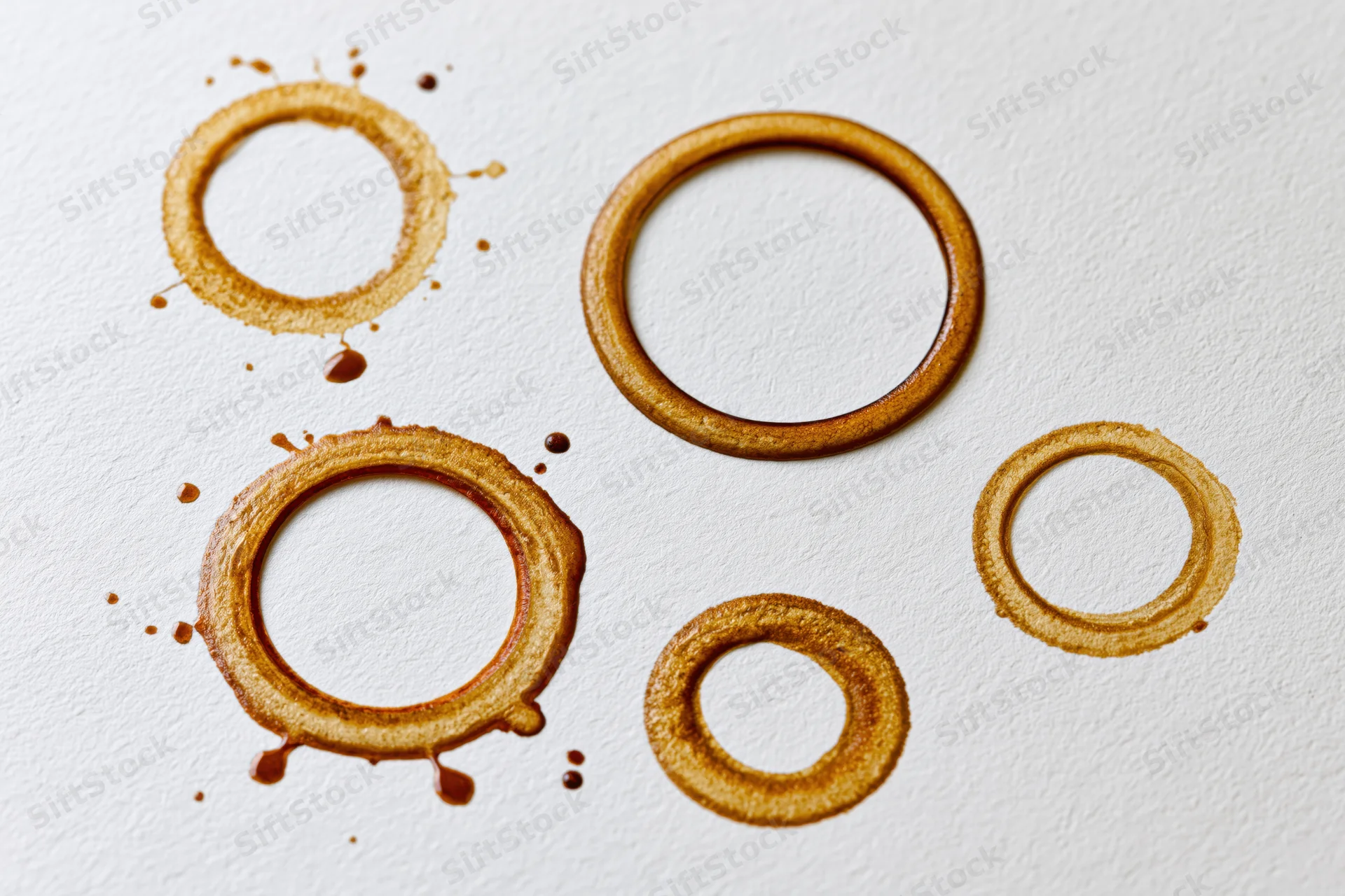 Coffee cup ring stains of varying sizes scattered across a white textured surface