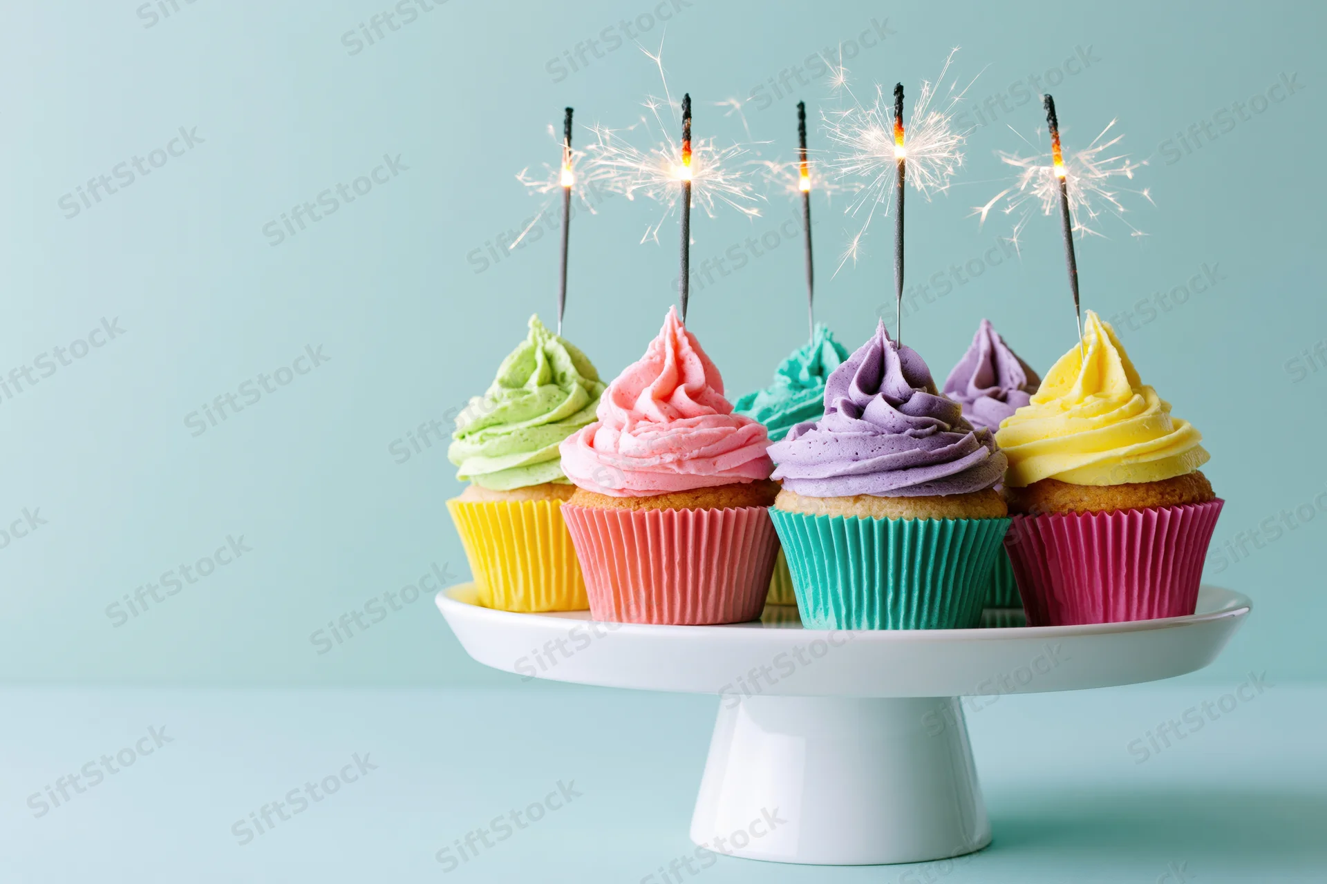 Colorful frosted cupcakes with sparklers on a white cake stand