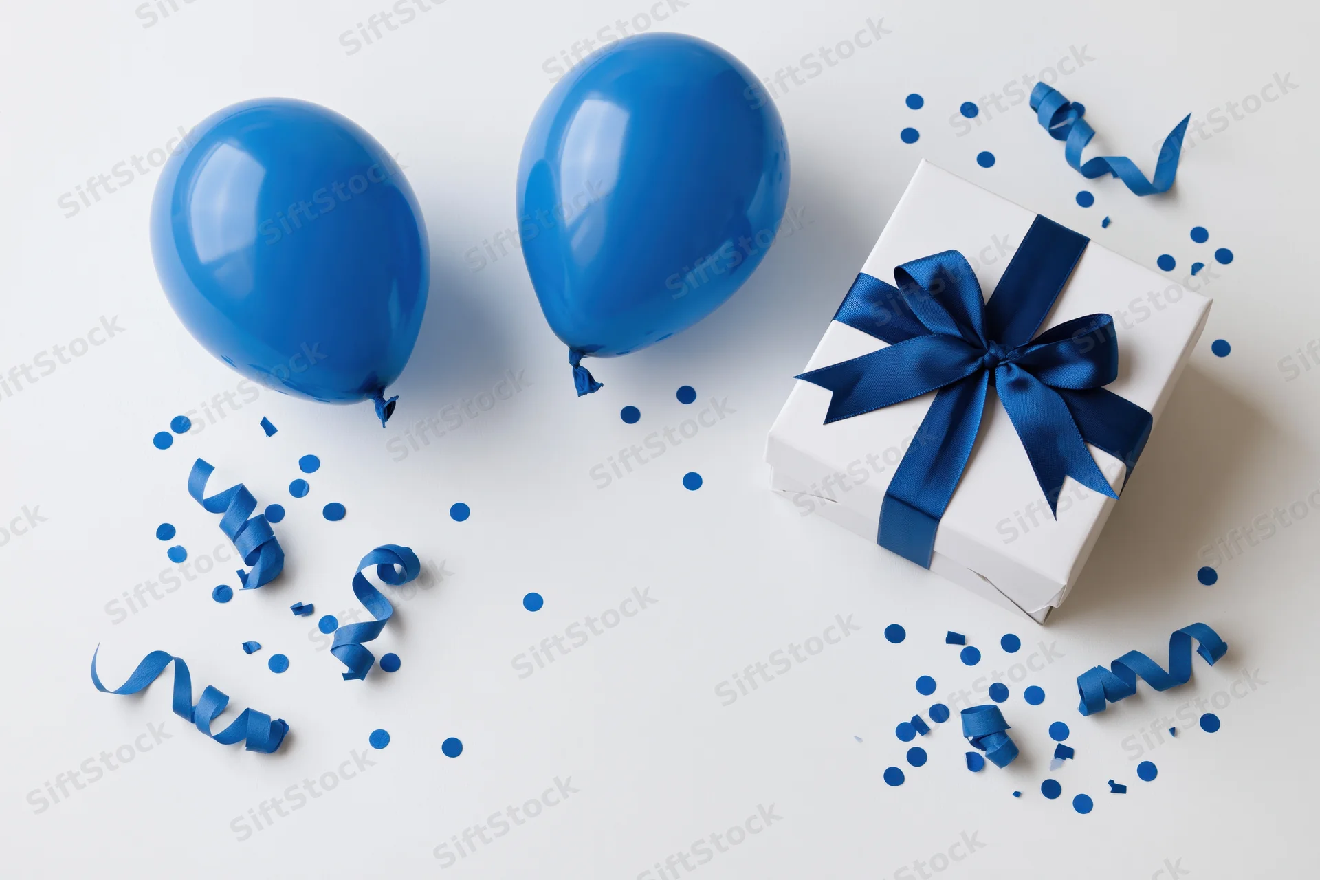 Blue balloons and a wrapped gift with confetti on a white surface