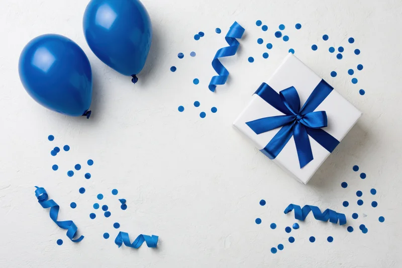 White gift box with blue ribbon and balloons on a clean surface