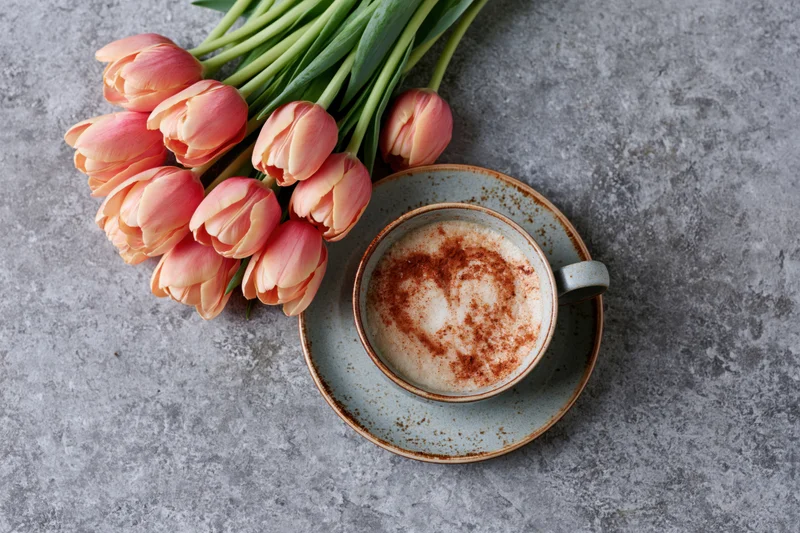 Ceramic cappuccino cup with cinnamon heart and pink tulips on gray surface