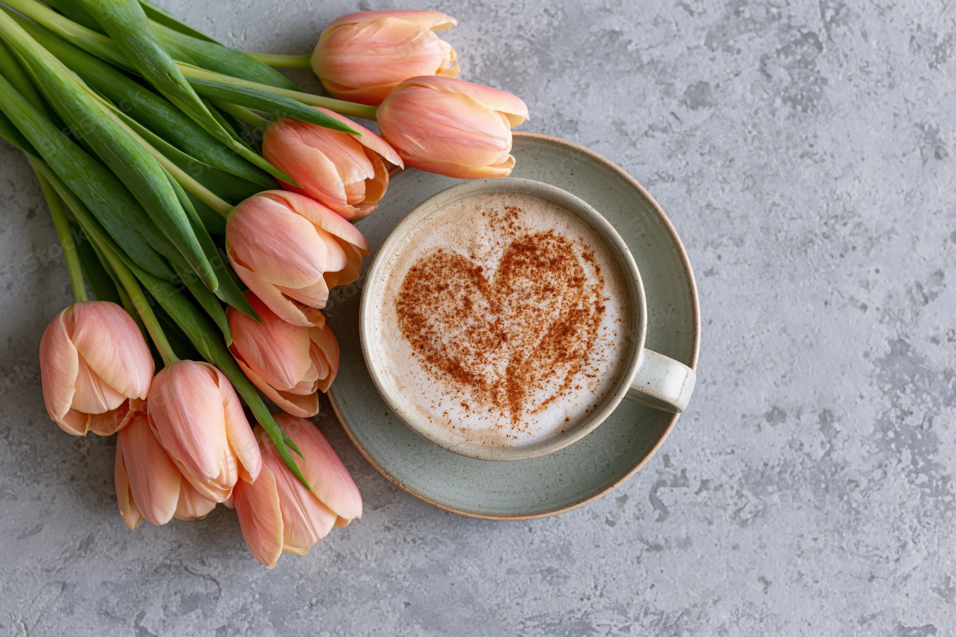 Ceramic cappuccino cup with cinnamon heart design and pink tulips on gray surface