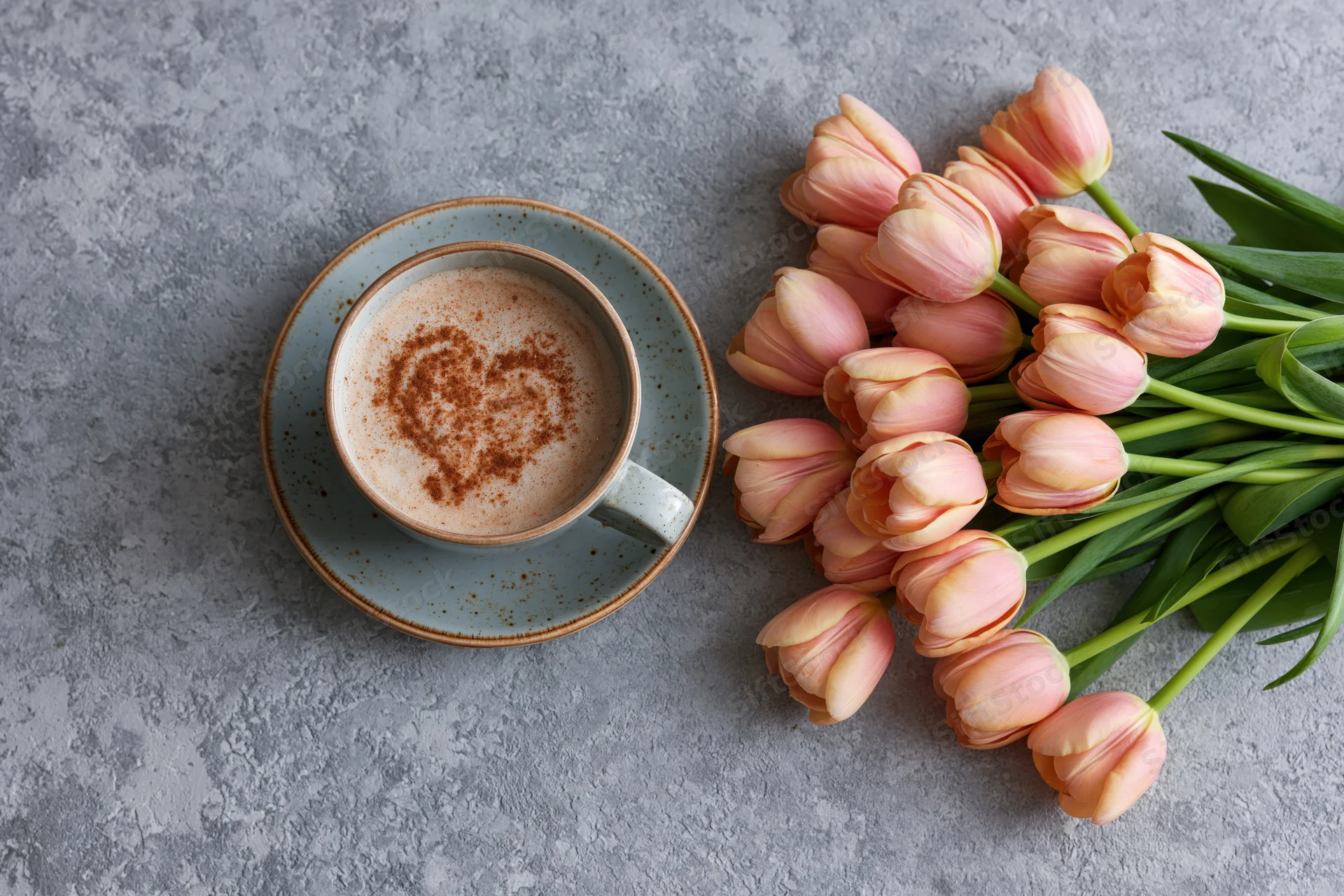 Ceramic cappuccino cup with cinnamon heart and pink tulips on gray concrete surface