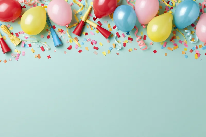 Colorful balloons and party decorations arranged in a flat lay at the top of a mint background with copyspace below