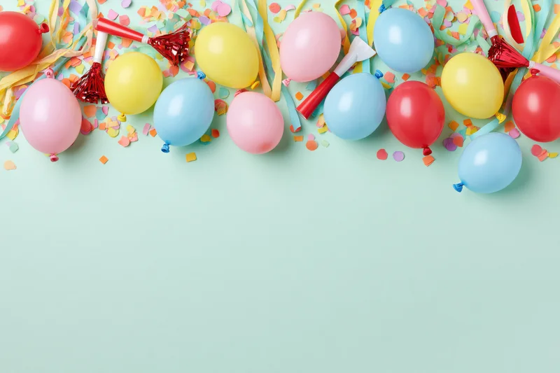 Colorful balloons and party supplies arranged in a flat lay on a mint background with copyspace below