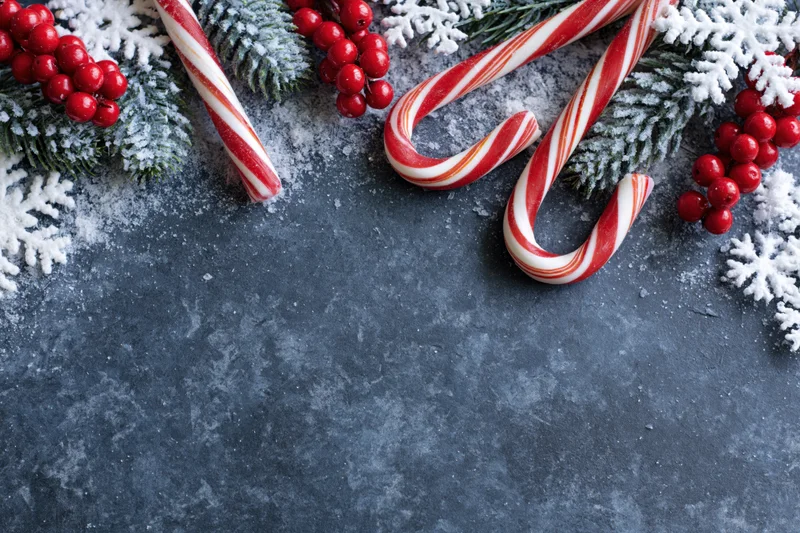 Candy canes and pine branches with red berries and snowflakes arranged along the top edge of a dark textured surface, leaving copyspace below