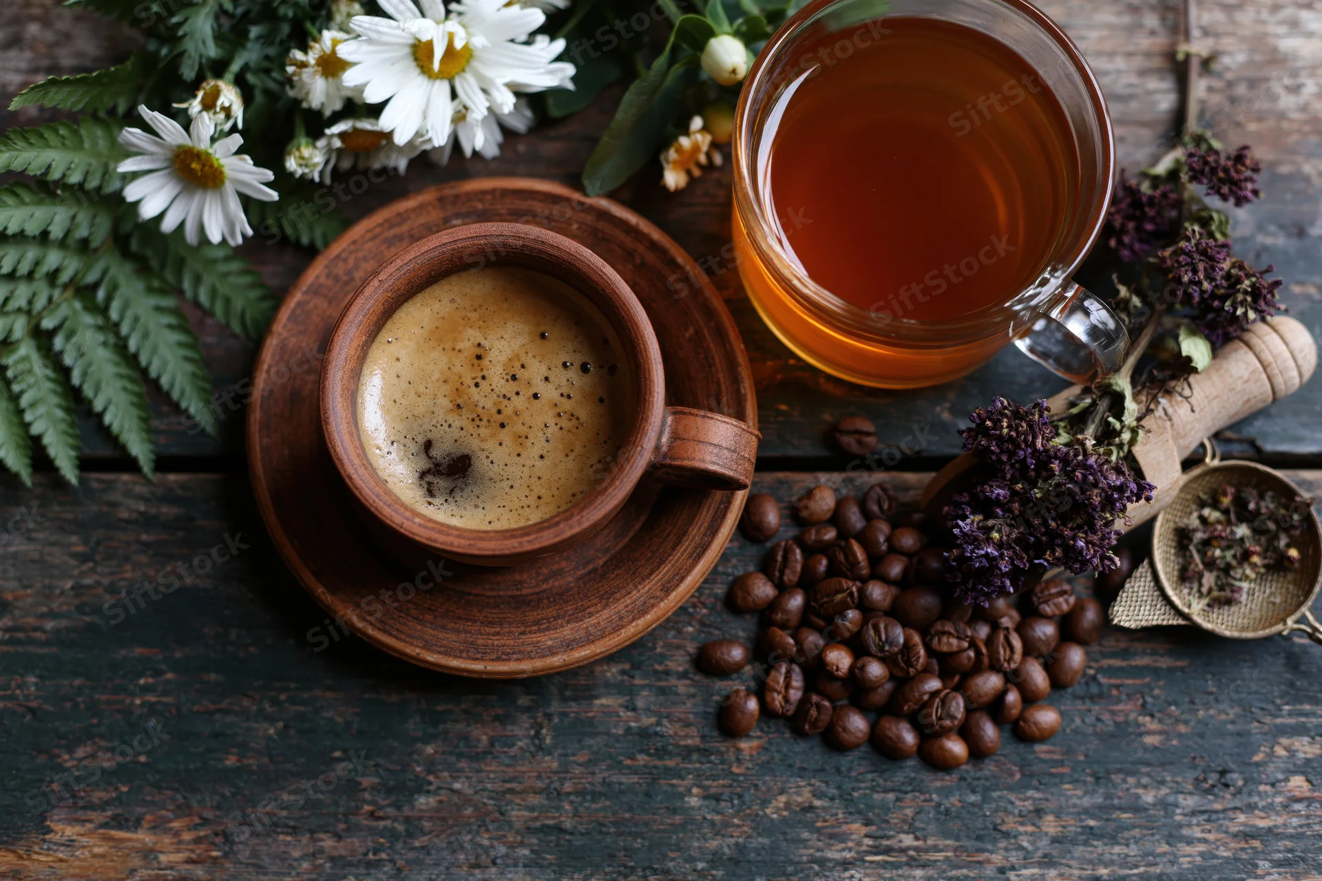 Terracotta coffee cup with saucer and scattered beans on dark wooden table beside glass tea mug and fresh flowers