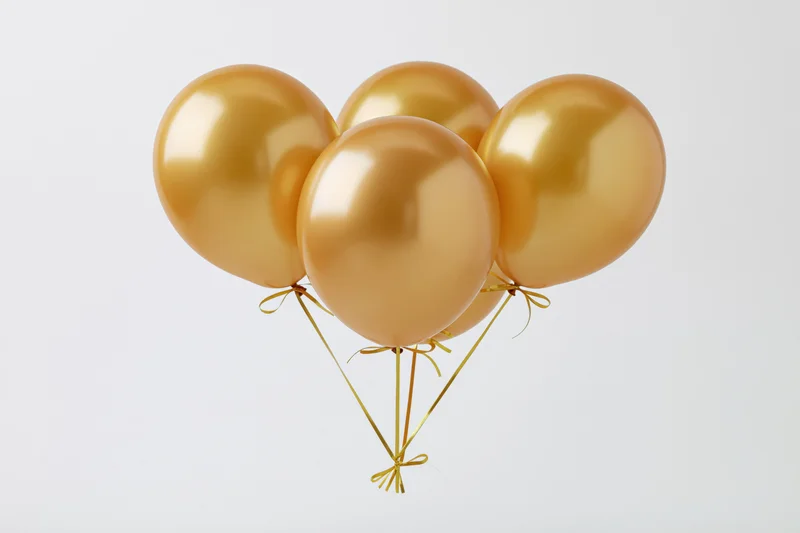 Four metallic gold helium balloons tied together floating against a white background
