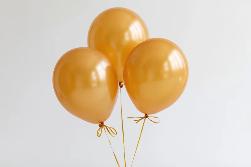 Four metallic gold helium balloons clustered together tied with ribbons against a white background