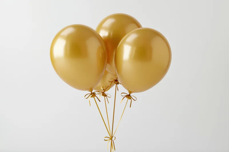 Four metallic gold helium balloons tied together floating against white background