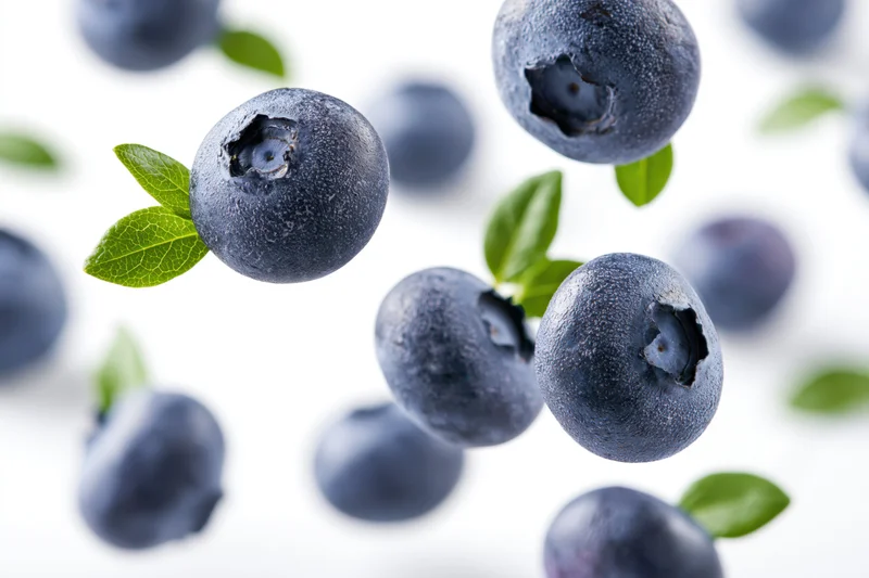 Blueberries floating midair with green leaves against white background