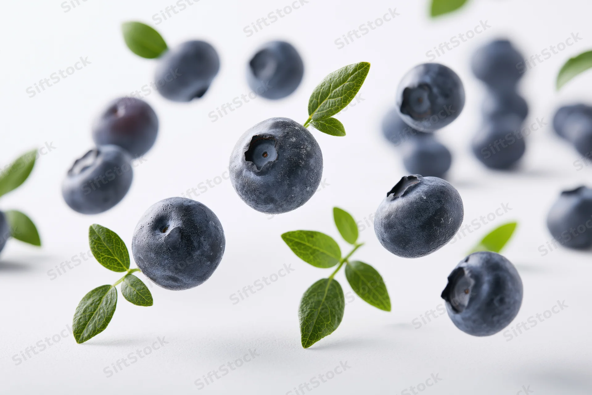 Blueberries floating midair with green leaves scattered on white surface