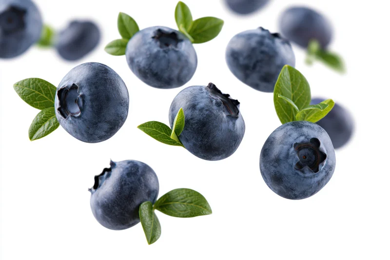 Blueberries floating midair with green leaves scattered on white background