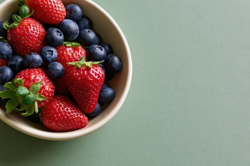 Strawberries and blueberries in a bowl on a green surface with copyspace