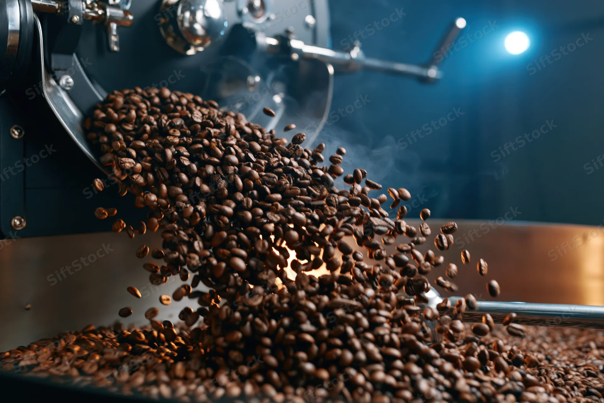 Roasted coffee beans cascading from a roasting machine into a drum in a factory setting