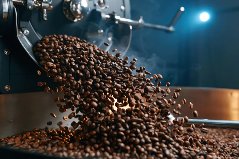 Roasted coffee beans cascading from a roasting machine into a drum in a factory setting
