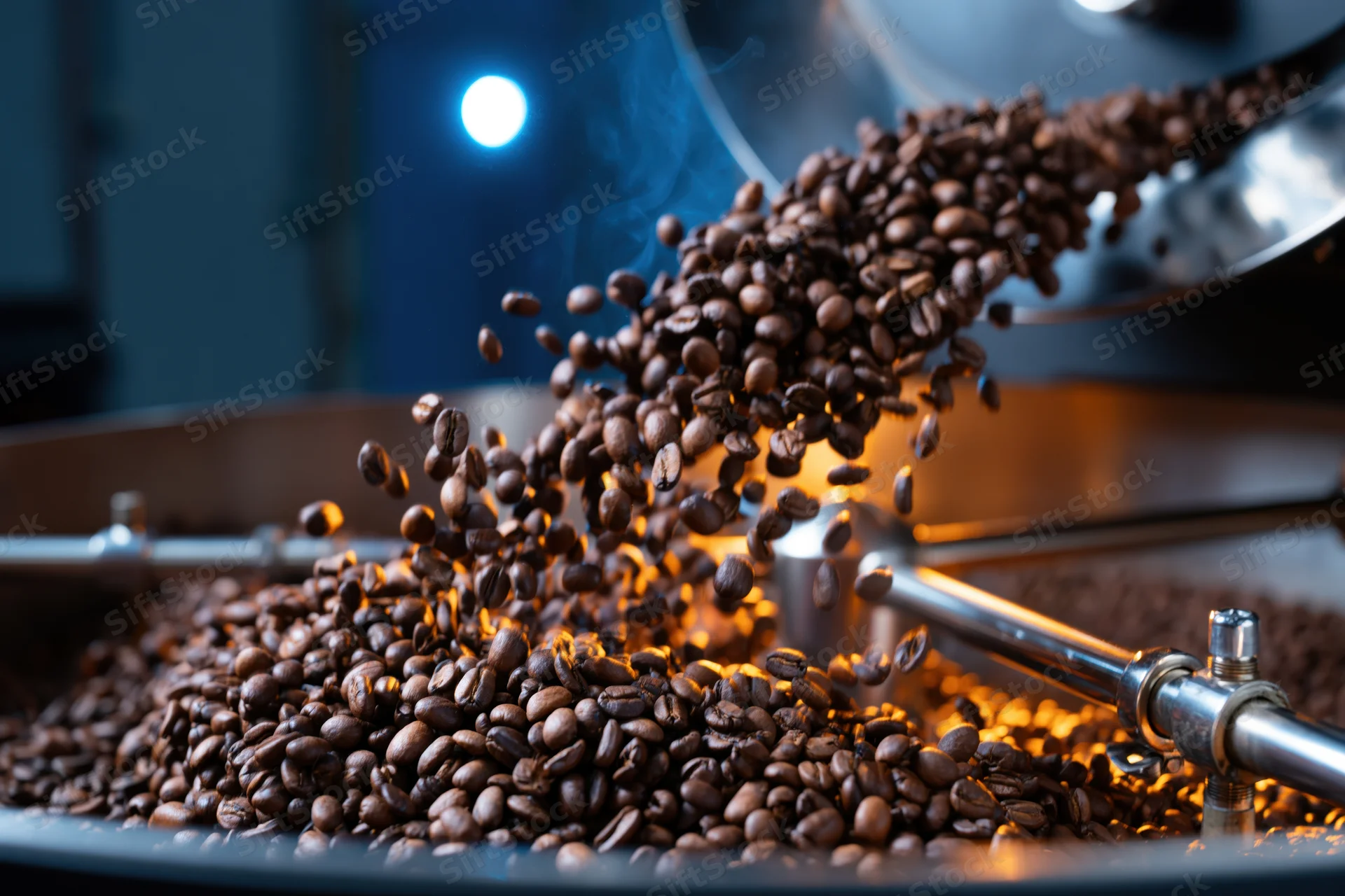 Roasted coffee beans cascading from a roasting machine into a metal tray in a factory setting