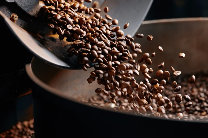 Roasted coffee beans cascading from a metal chute into a container during roasting process