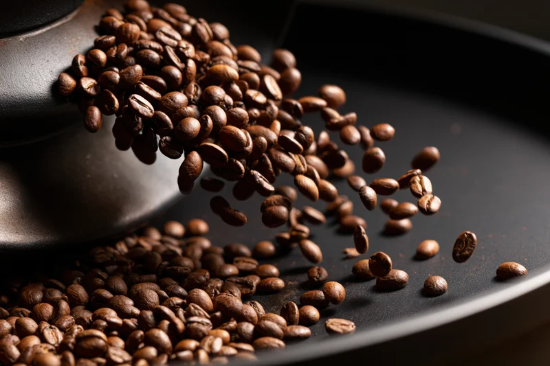 Roasted coffee beans cascading from a matte ceramic container onto a dark surface