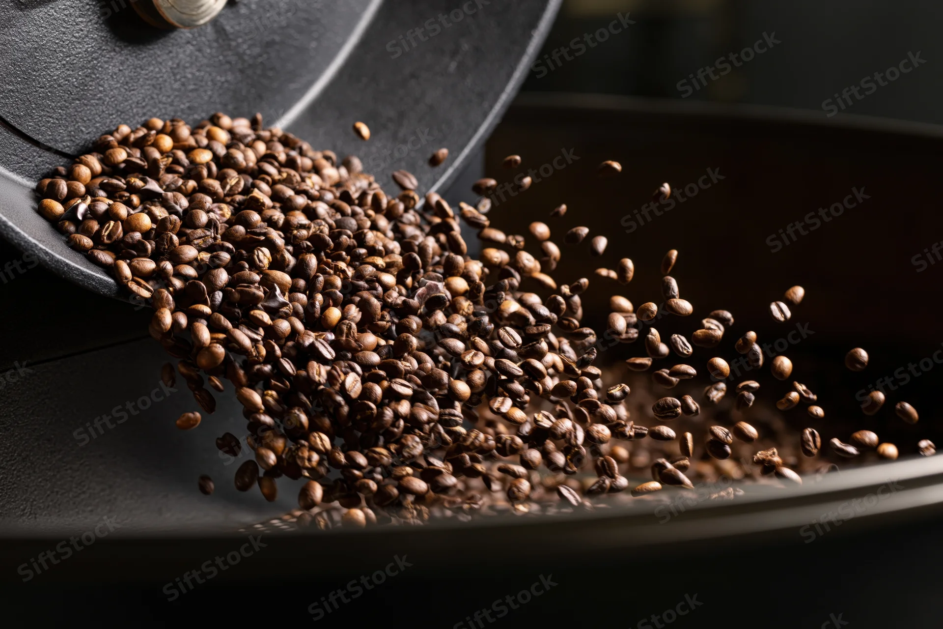Roasted coffee beans cascading from a matte black container into a tray