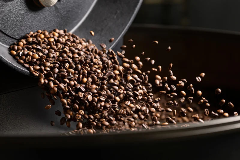 Roasted coffee beans cascading from a matte black container into a tray