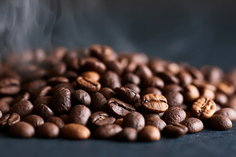 Freshly roasted coffee beans steaming on a dark surface