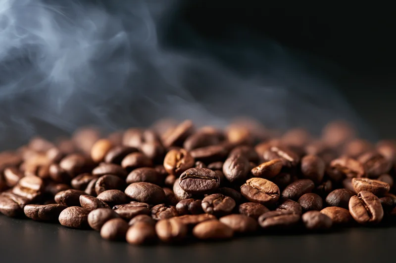 Freshly roasted coffee beans steaming on a dark surface
