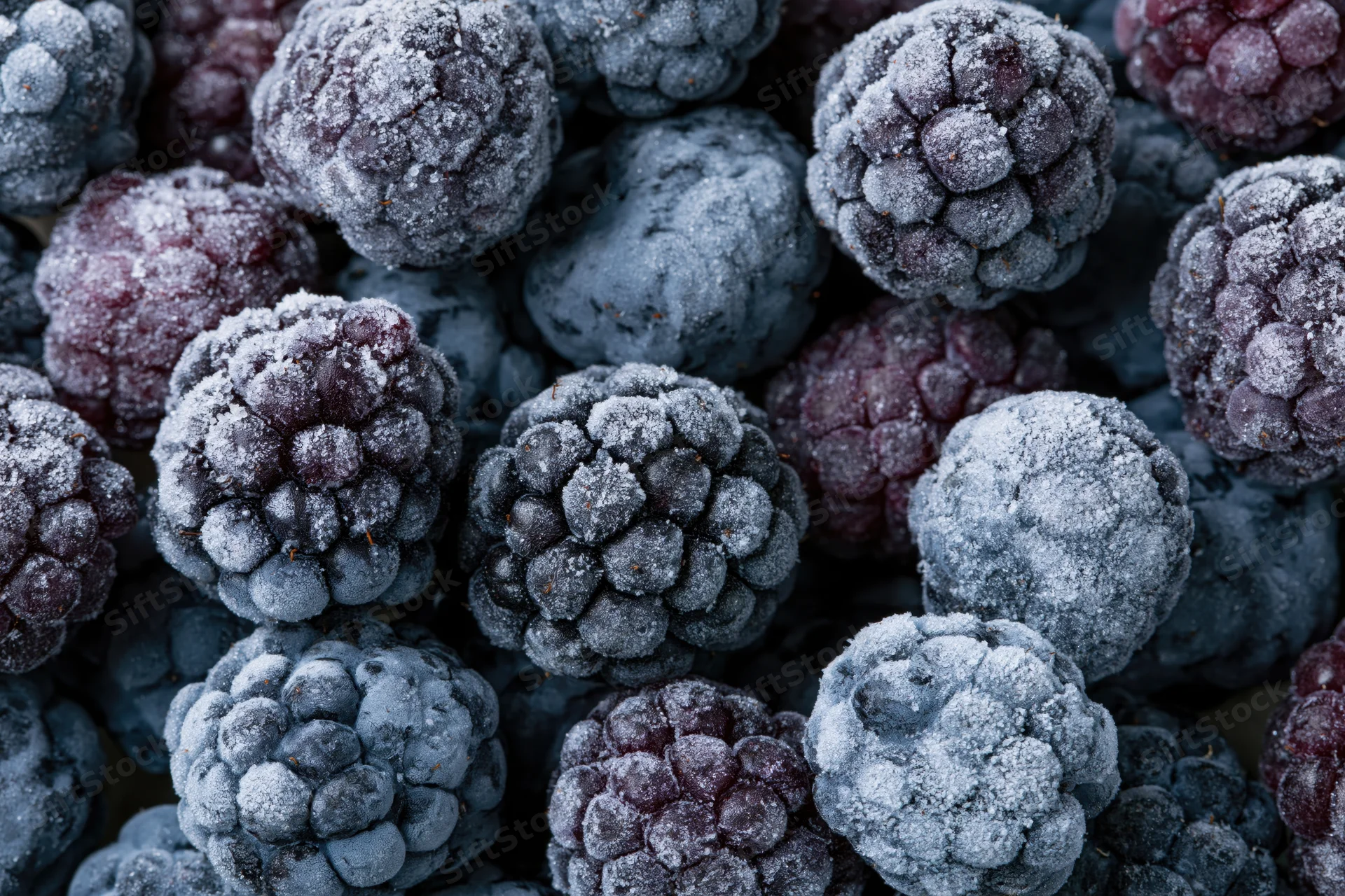 Frozen blackberries covered in frost, tightly packed in a close-up view