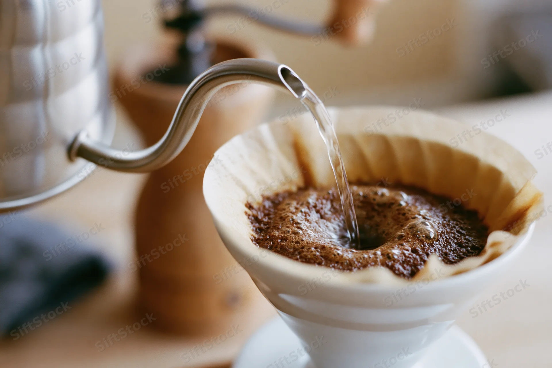 Hot water pouring from a gooseneck kettle into a paper filter filled with coffee grounds on a wooden surface