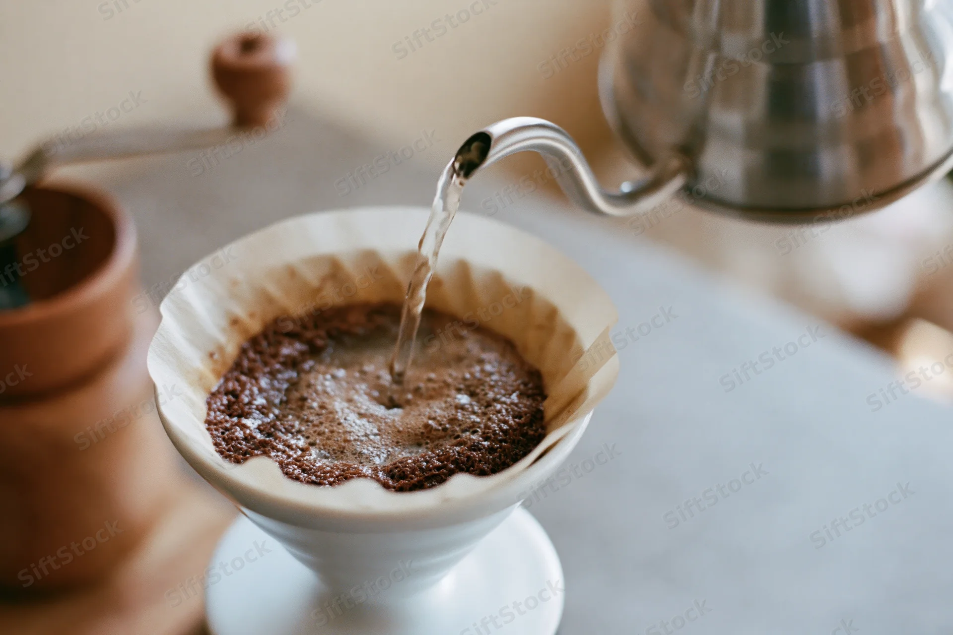 Hot water pouring from a gooseneck kettle into a paper filter filled with coffee grounds on a countertop