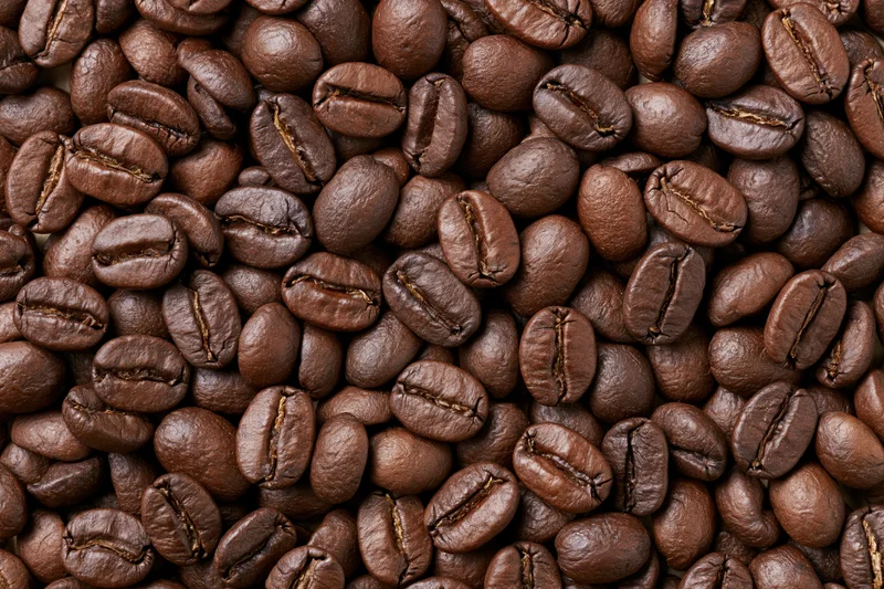 Roasted coffee beans densely spread across a flat surface in closeup view