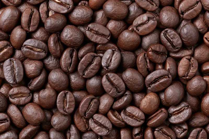 Roasted coffee beans densely spread in a closeup view showing texture and rich brown color