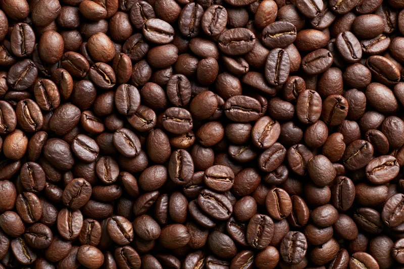Roasted coffee beans densely spread across a flat surface in closeup view