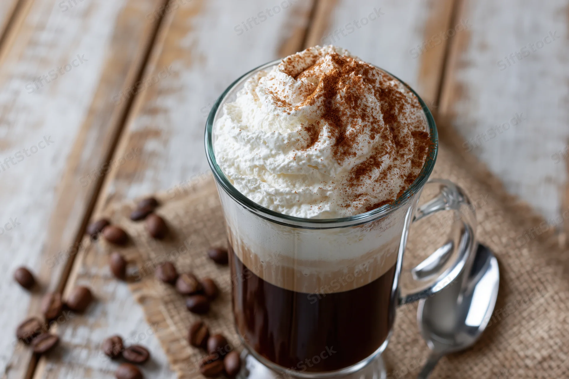 Tall glass mug of layered irish coffee with whipped cream and cinnamon on wooden table