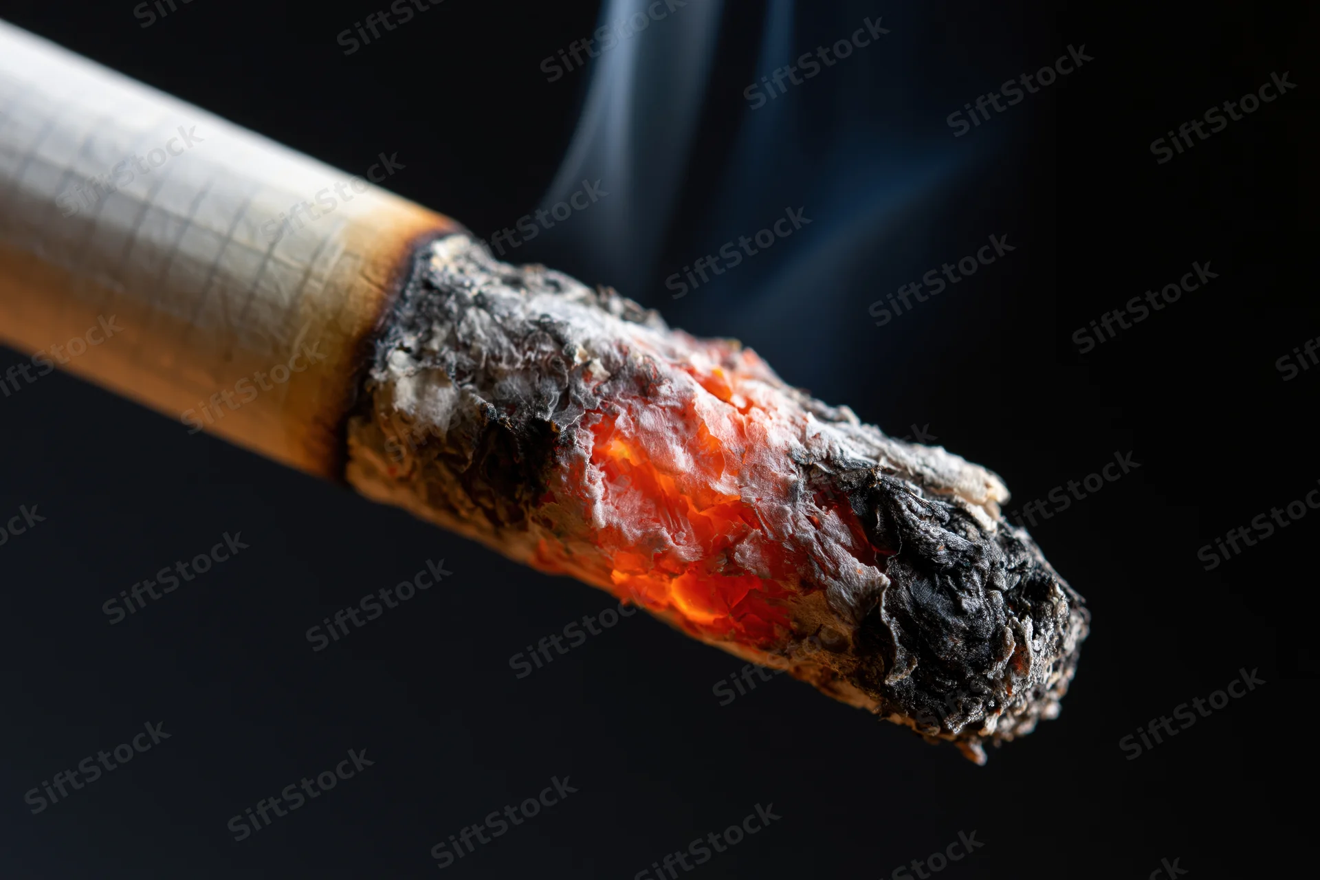 Burning cigarette tip with glowing ember and rising smoke against dark background