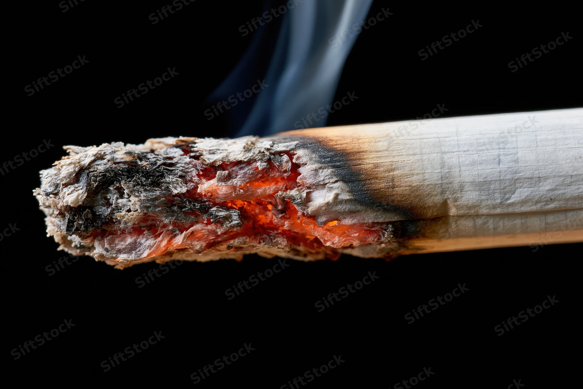 Burning cigarette tip with glowing ember and rising smoke against black background