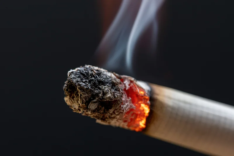 Burning cigarette tip with glowing ember and rising smoke against dark background