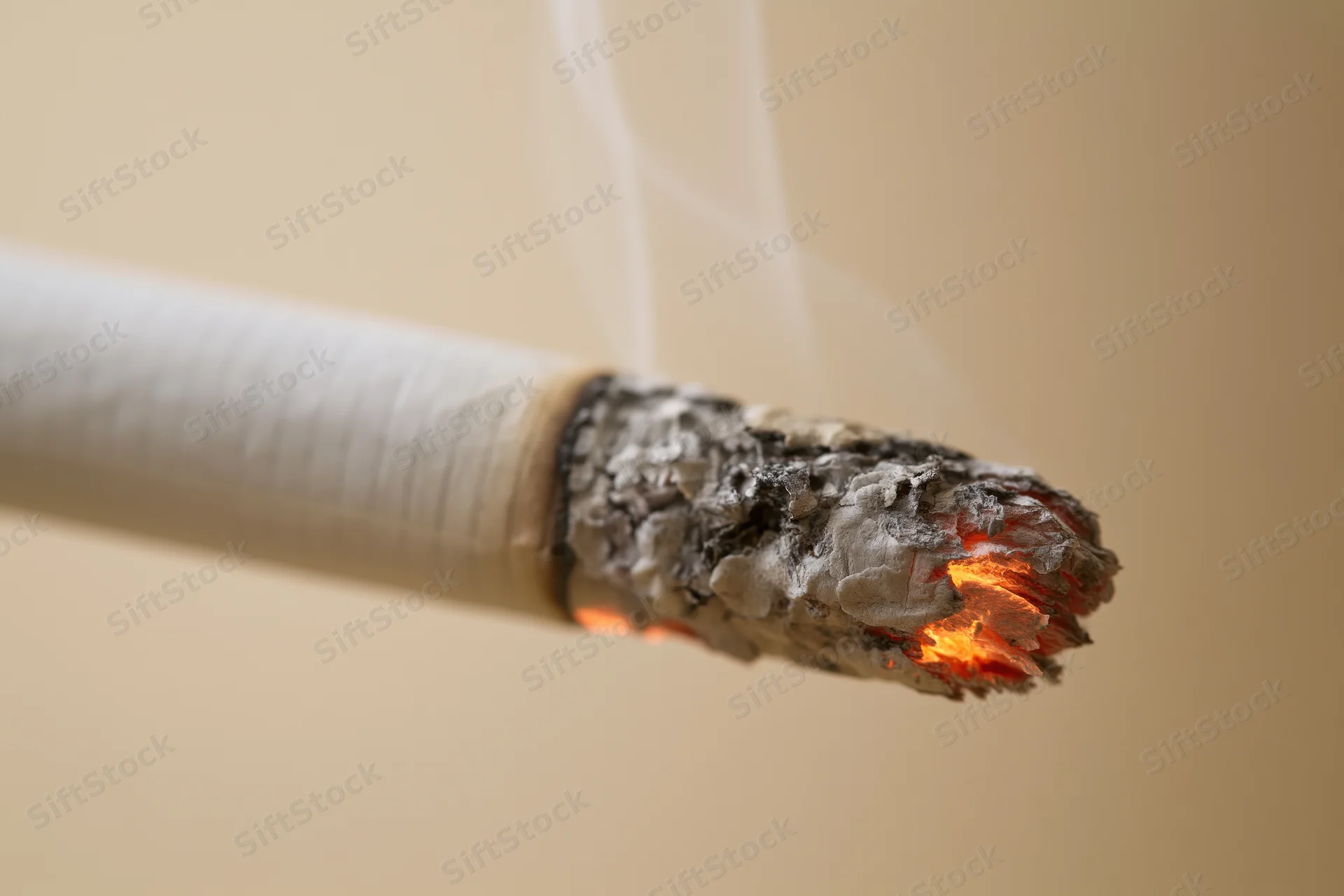 Lit cigarette tip glowing with orange ember and rising smoke against plain background