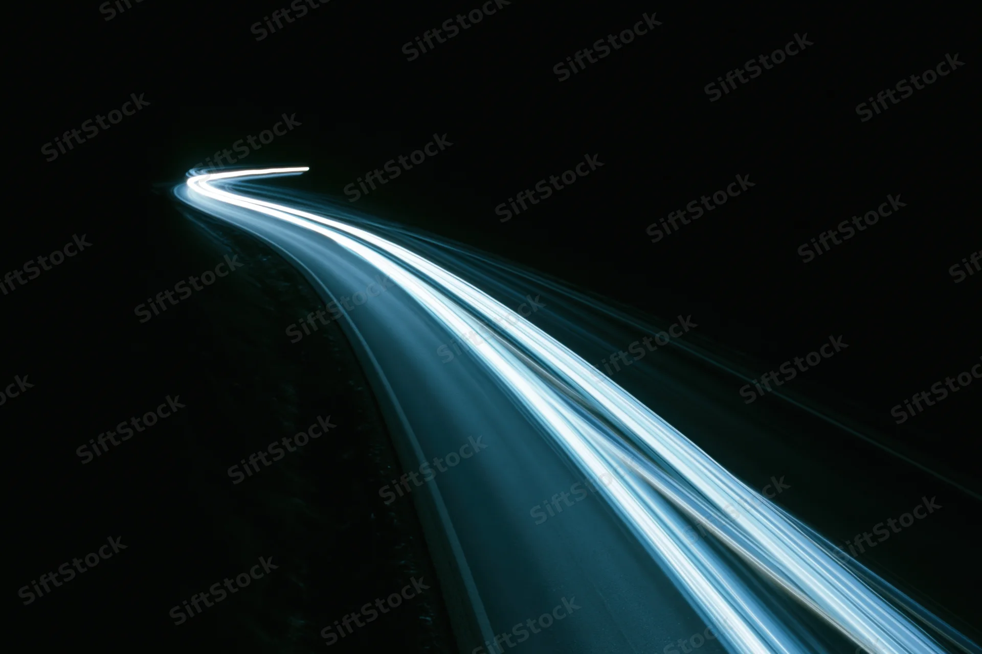 Long-exposure night highway with light trails from moving vehicles curving into darkness