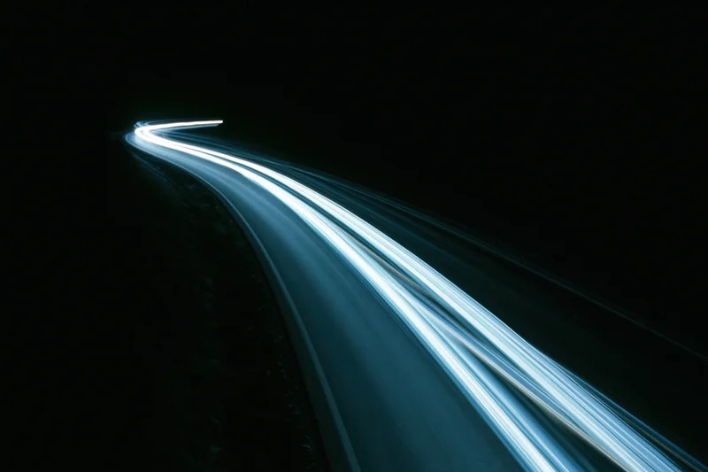 Long-exposure night highway with light trails from moving vehicles curving into darkness