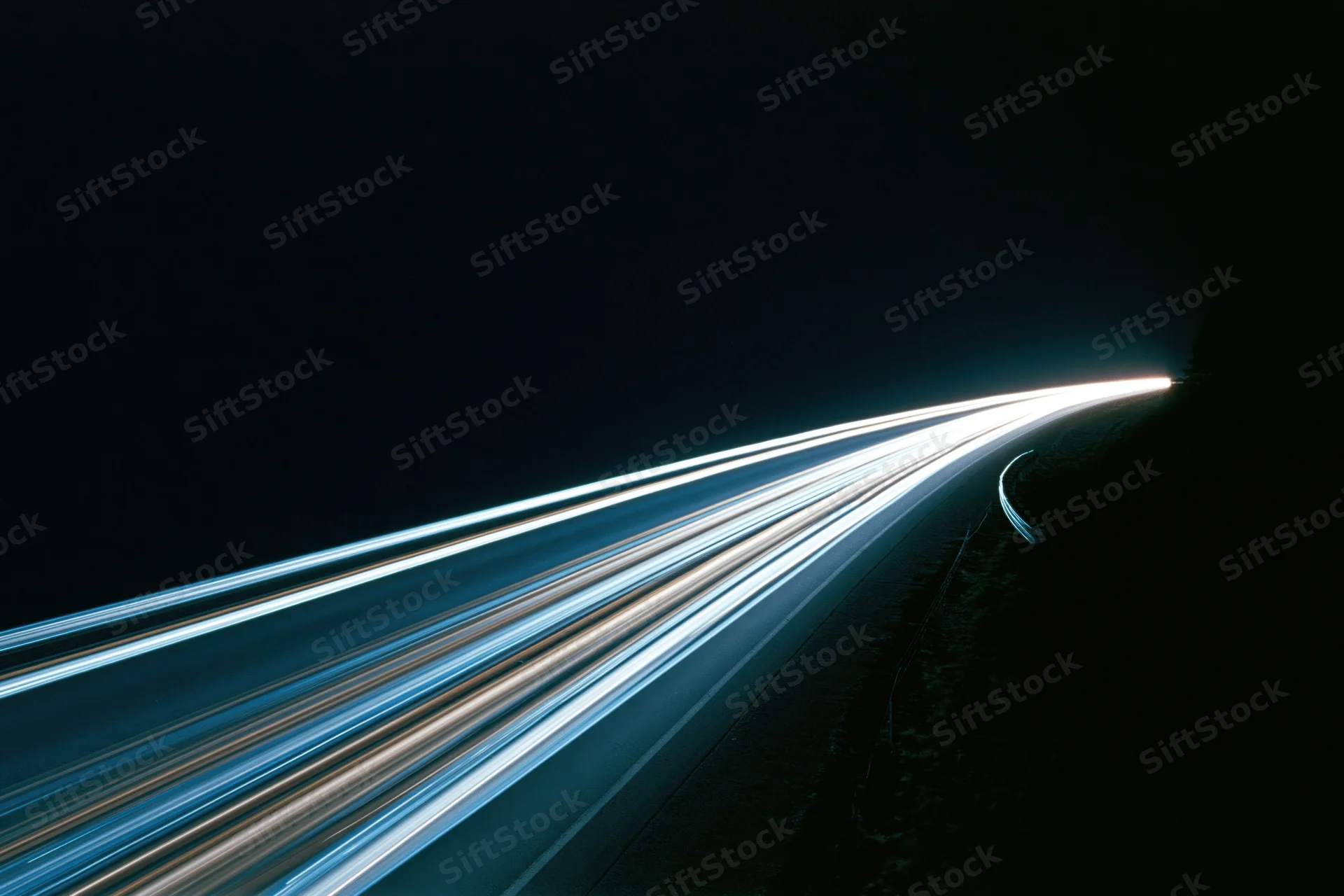 Long-exposure night highway with light trails from moving vehicles curving into the distance