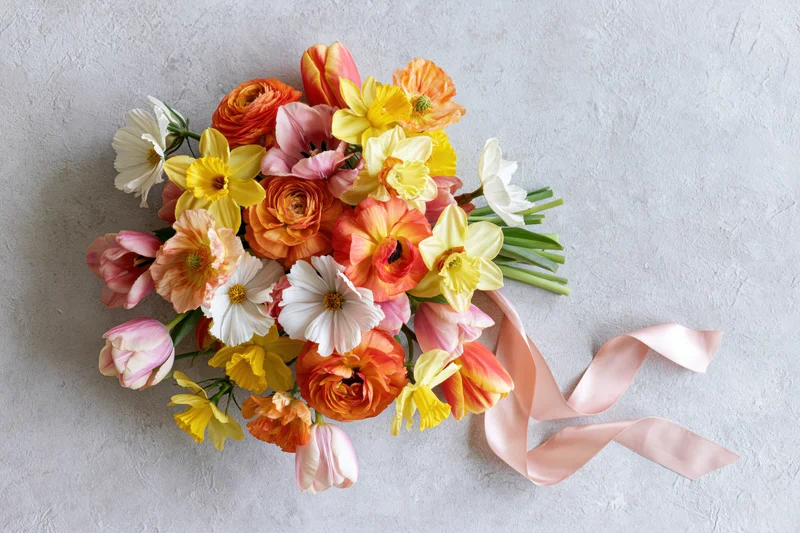 Heart-shaped bouquet of spring flowers with pink ribbon on light textured surface