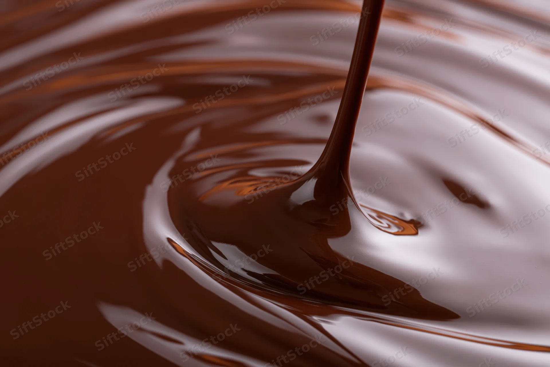 Melted dark chocolate pouring in a thin stream creating ripples on a glossy surface