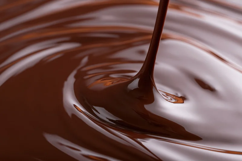 Melted dark chocolate pouring in a thin stream creating ripples on a glossy surface